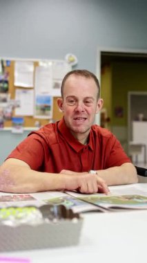 Zihinsel engelli bir adam, bir gündüz merkezindeki etkinlik oturumunda yaratıcı veya öğrenme görevine katılırken duygu ve bağlılığını ifade ederek neşe içinde tepki verir.