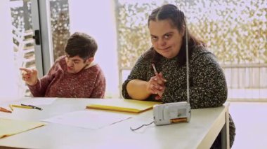 Zihinsel engelli iki mutlu kadın asistan zihinsel sağlık merkezindeki bir masada çizim ve renklendirme faaliyetlerine odaklanarak, bilişsel gelişim faaliyetlerine katkı ve konsantrasyon göstermektedir.