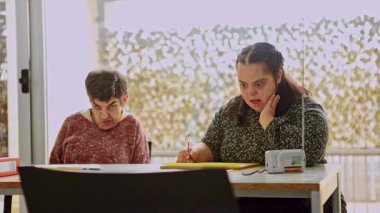 Zihinsel engelli iki kadın vatandaş, zihinsel gelişim faaliyetlerine katkı ve konsantrasyon göstererek, zihinsel sağlık merkezindeki bir masada çizim ve renklendirme faaliyetlerine odaklanmıştır.