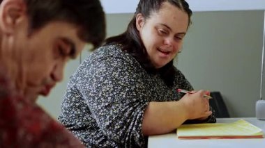 Zihinsel engelli iki mutlu kadın asistan zihinsel sağlık merkezindeki bir masada çizim ve renklendirme faaliyetlerine odaklanarak, bilişsel gelişim faaliyetlerine katkı ve konsantrasyon göstermektedir.