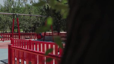 Issız bir oyun parkında, dingin bir parkta canlı kırmızı ve mavi ekipmanlar bulunur. Bu da çocuksuz sakin bir günü işaret eder..