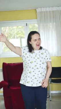 Down sendromlu bir kadın, bir akıl hastanesinin parlak ışıklı odasında dans ederken neşe ve coşku ifade eder. Dinamik duruşu ve coşkulu ifadesi bir mutluluk ve özgürlük anını temsil ediyor..