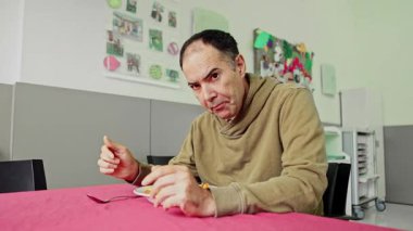 Zihinsel engelli orta yaşlı bir adamın akıl hastanesinde tek başına yemek yediği resmedilmiştir. Bir kaşığı tutarken odaklanmış bir yüz ifadesi gösteriyor..