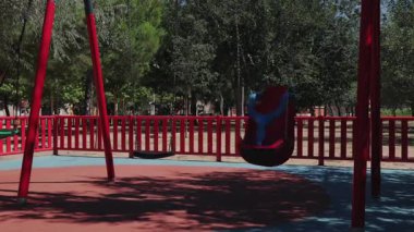 Kırmızı salıncakların ve ağaçlarla çevrili renkli ekipmanların gerçek zamanlı çekildiği boş bir oyun alanı..