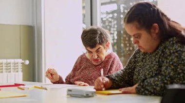 Zihinsel engelli iki kadın vatandaş, zihinsel gelişim faaliyetlerine katkı ve konsantrasyon göstererek, zihinsel sağlık merkezindeki bir masada çizim ve renklendirme faaliyetlerine odaklanmıştır.