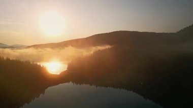 Karadağ 'ın sisle kaplanmış sakin bir göl üzerinde doğan güneşinin büyüleyici hava görüntüsü. Güneş ışığı manzarayı aydınlatıyor, sakin sabah atmosferini vurguluyor..