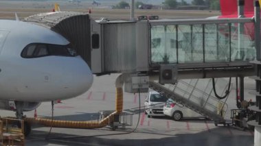 Havaalanı kapısına yanaşmış bir uçak yolcu indirmeye ya da binmeye hazır bir jet köprüsüne bağlanmış. Olay yeri havaalanı operasyonlarını canlı çekiyor..