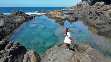 Hava aracı Fuerteventura, Kanarya Adaları 'ndaki Aguas Verdes' teki doğal yüzme havuzlarında dinlenen tanınmayan bir kadını yakalıyor. Engebeli arazi turkuaz suları çevrelemektedir..