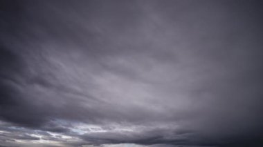 Gökyüzünü karartan fırtına bulutlarının dinamik hareketlerini gösteren bir zaman dilimi videosu, ufukta beliren sönük bir parıltıyla tezat oluşturuyor..