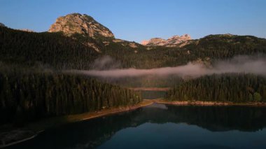Karadağ 'ın bereketli ormanları ve sabahın erken saatlerindeki ışığı yansıtan sakin bir gölle örtülü sakin manzarasının çarpıcı bir hava manzarası görülüyor.