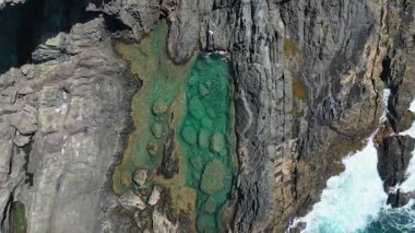 Fuerteventura, Kanarya Adaları 'ndaki Aguas Verdes doğal yüzme havuzlarının en üst görüntüsü engebeli kaya oluşumlarıyla çevrili turkuaz suları betimlemektedir. Tanımlanamayan bir kadın havuzda yüzüyor. Hava aracının perspektifinden çekilmiş..