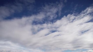 Beyaz bulutların parlak mavi gökyüzüne doğru hızlı bir şekilde hareket ettiğini gösteren zaman dilimi videosu, hava modellerini ve hareket halindeki doğal manzarayı resmetmek için idealdir..