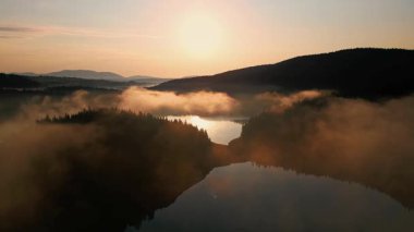 Karadağ 'ın güneşin doğuşundaki gür manzarasının sakin havası, sakin suların üzerindeki sisi ve yumuşak bir sabah parıltısının altındaki uzak tepelerin siluetini yakalıyor.