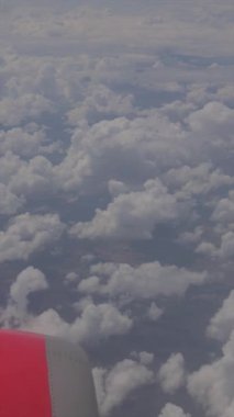 Temiz bir gökyüzünün altında geniş, tüylü, beyaz bulutları gösteren bir hava manzarası. Görüntü, seyahat perspektifi sunan kırmızı bir uçak kanadının bir parçasını içeriyor..