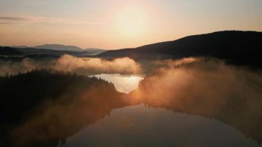 Karadağ 'ın büyüleyici hava manzarası, gün doğumunda yemyeşil ormanlarla çevrili sis kaplı bir gölü gösteriyor. Altın ışık suyu yansıtıyor, huzurlu bir sahne yaratıyor..