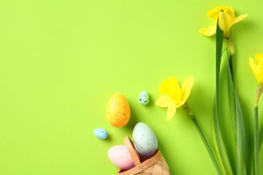 İçinde renkli Paskalya yumurtaları ve yeşil masanın üzerinde nergis çiçekleri olan sepet. Mutlu Paskalya bayrağı tasarımı.