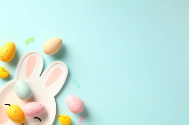 Paskalya tebrik kartı şablonunuz kutlu olsun. Renkli Paskalya yumurtaları ve pastel mavi arka planda tavşan şeklinde tabaklar..