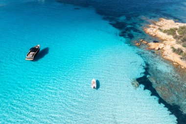 Yazın mavi denizde güzel lüks bir yat ve tekne manzarası. Sardunya, İtalya. Sürat teknesi, deniz kıyısı, şeffaf gök mavisi. Seyahat et. Tropik bir manzara. Yatçılık. Deniz Burnu