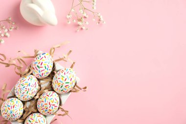 Mutlu Paskalyalar. Tatlı Paskalya yumurtaları, tavşancık ve pembe masadaki bahar çiçekleri. Düz konum, üst görünüm, kopyalama alanı.