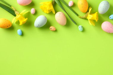 Renkli Paskalya yumurtaları ve yeşil masadaki sarı bahar çiçeklerinden oluşan mutlu Paskalya çerçeveleri. Paskalya tebrik kartı şablonu, pankart tasarımı. Düz konum, üst görünüm, kopyalama alanı.
