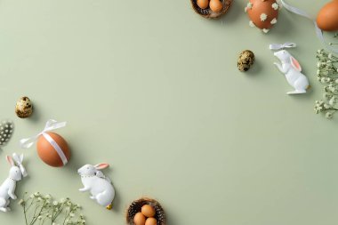 Paskalya düzlüklerinde dekoratif yumurtalar, seramik tavşanlar ve pastel yeşil arka planda çiçekler vardı.