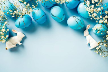 Mavi Paskalya yumurtaları, çiçekler, mavi arka planda tavşanlar. Düz konum, üst görünüm, kopyalama alanı.