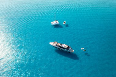 Yazın mavi denizde güzel lüks bir yat ve tekne manzarası. Sardunya, İtalya. Sürat teknesi, deniz kıyısı, şeffaf gök mavisi. Seyahat et. Tropik bir manzara. Yatçılık. Deniz Burnu