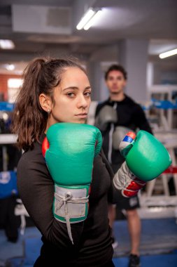 Kararlı kadın boksör yeşil boks eldiveni giyiyor. Bir boks ringinde güven içinde poz veriyor. Gücünü ve bağlılığını bu spora gösteriyor.
