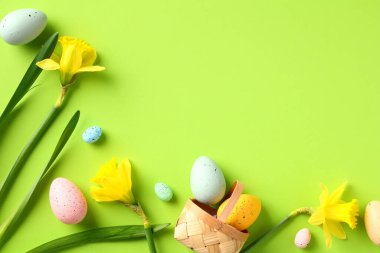 Mutlu Paskalya kompozisyonu. Renkli Paskalya yumurtaları ve yeşil arka planda sarı nergis çiçekleri..