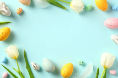 Mutlu Paskalya tebrik kartı tasarımları. Lalelerden yapılmış çerçeve bahar çiçekleri, tavşan süslemeleri, pastel mavi arka planda renkli Paskalya yumurtaları..