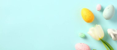 Mutlu Paskalya bayrağı, mesaj için yer var. Renkli Paskalya yumurtaları, beyaz lale, pastel mavi arka planda Paskalya tavşanı..