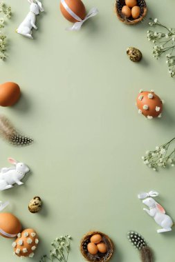 Mutlu Paskalya bayrağı tasarımı. Kahverengi Paskalya yumurtalarının çerçevesi süslü çiçekler, bıldırcın yumurtaları, pastel yeşil arka planda seramik tavşanlar. Düz konum, üst görünüm, kopyalama alanı.
