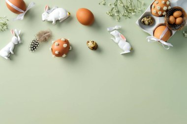 Zarif Paskalya bezi. Paskalya yumurtaları, bahar çiçekleri, pastel yeşil arka planda seramik tavşanlar. Düz yatış, üst görünüm.