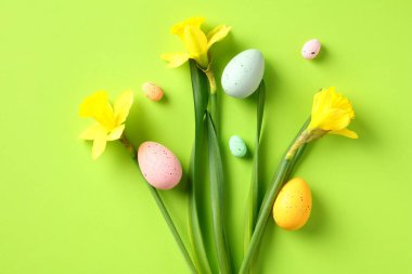 Renkli Paskalya yumurtaları ve yeşil arkaplanda nergis çiçekleri. Mutlu Paskalya tebrik kartları. Düz yatış, üst görünüm.