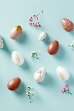 Paskalya kompozisyonu. Paskalya yumurtaları, çiçek, pastel mavi arka planda dekoratif tavşanlar. Düz yatış, üst görünüm