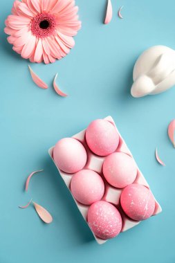 Pembe Paskalya yumurtaları, tavşancık, bahar çiçeği, turkuaz arka planda taç yaprakları. Düz, üst görünüm, moda renkler.