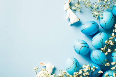 Şirin Paskalya yumurtaları, çiçekler, mavi arka planda dekoratif tavşanlar. Düz konum, üst görünüm, kopyalama alanı. Mutlu Paskalya kartı tasarımı.