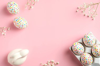 Mutlu Paskalyalar. Renkli benekli Paskalya yumurtalarından yapılmış çerçeve, bahar çiçeği, pembe arka planda Paskalya tavşanı. Düz konum, üst görünüm, kopyalama alanı.
