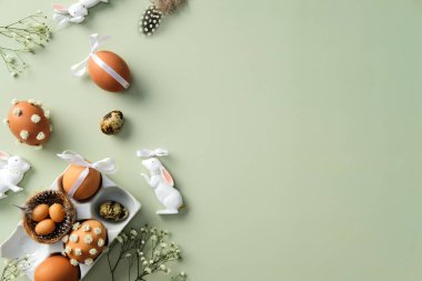 Paskalya düz kompozisyonu dekore edilmiş yumurtalar, seramik tavşanlar ve pastel yeşil arka planda çiçekler.