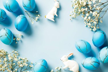 Mavi Paskalya yumurtaları, tavşancık, açık mavi arka planda çiçekler. Mutlu Paskalya tebrik kartı şablonları. Düz konum, üst görünüm, kopyalama alanı.