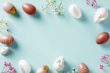Mutlu Paskalya tebrik kartı maketleri. Paskalya yumurtaları, minimalist çiçekler, pastel mavi arka planda dekoratif tavşanlar. Düz yatış, üst görünüm.