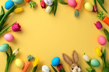 Mutlu Paskalyalar. Renkli Paskalya yumurtaları, laleler ve sarı arka planda şirin bir tavşan çerçevesi.