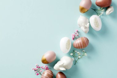 Şık Paskalya yumurtaları, minimalist çiçekler, pastel mavi arka planda dekoratif tavşanlar. Paskalya tebrik kartı tasarımı. Düz yatış, üst görünüm.