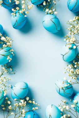 Düz kompozisyonda mermer Paskalya yumurtaları ve bahar çiçekleriyle mavi arka planda yatıyordu.