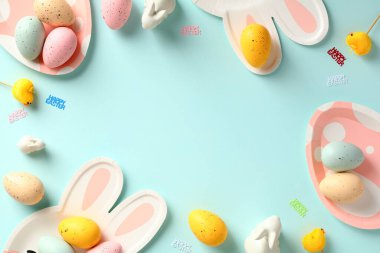 Paskalya çerçevesi sınırında renkli Paskalya yumurtaları, tavşancık ve yumurta şekilli çatal bıçak ve pastel mavi masa..
