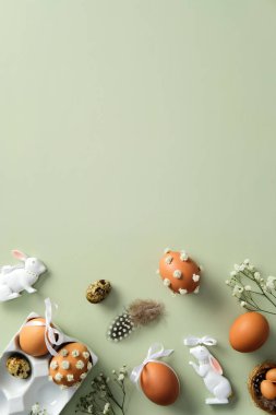 Mutlu Paskalya zarif dikey afiş tasarımı. Kahverengi Paskalya yumurtaları çiçekleri, bıldırcın yumurtaları, pastel yeşil arka planda seramik tavşanlar. Düz yatış, üst görünüm
