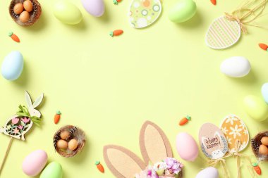Mutlu Paskalya tebrik kartı şablonları. Renkli Paskalya yumurtalarından yapılmış çerçeve, ahşap süslemeler, açık yeşil arka planda tavşan kulakları. Düz yatış, üst görünüm.