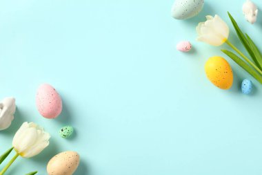 Mutlu Paskalya tebrik kartları. Pastel mavi arka planda laleler ve Paskalya yumurtaları. Düz yatış, üst görünüm.