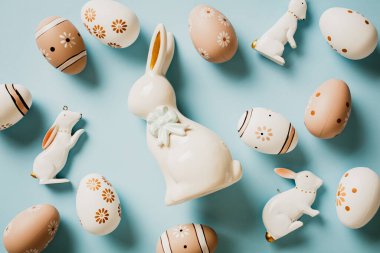 El yapımı dekoratif yumurtaları ve pastel mavi arka planda tavşanları olan seramik Paskalya tavşanı. Mutlu Paskalyalar. Düz yatış, üst görünüm.
