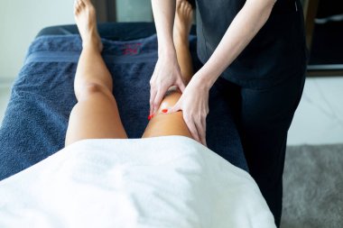 Profesyonel masöz nemlendirici krem sürüyor ve spa ya da güzellik merkezindeki müşteriye rahatlatıcı bacak masajı yapıyor.
